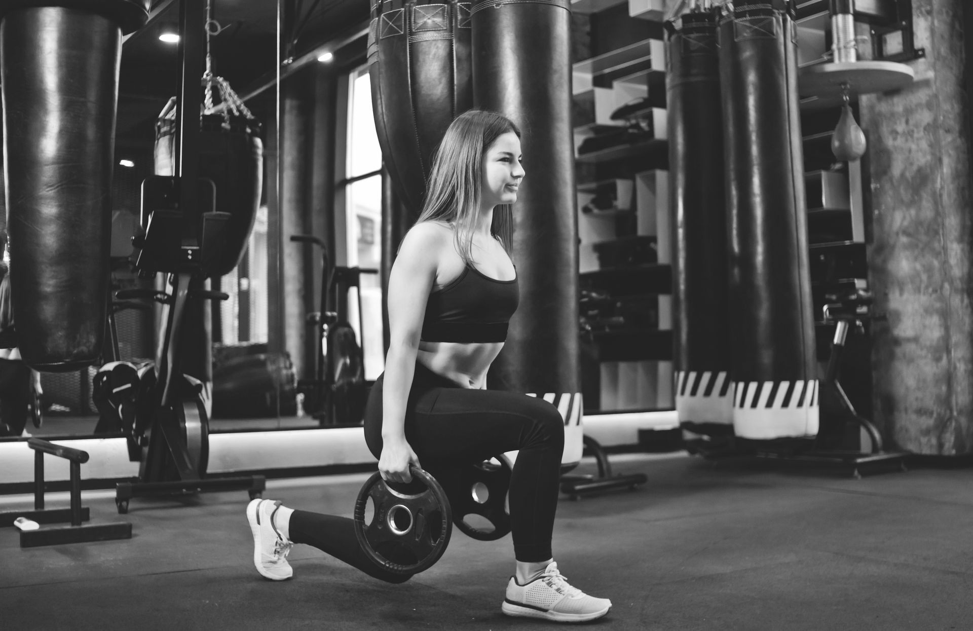 Training legs in the gym. Attractive fit woman doing lunges with discs from the bar.