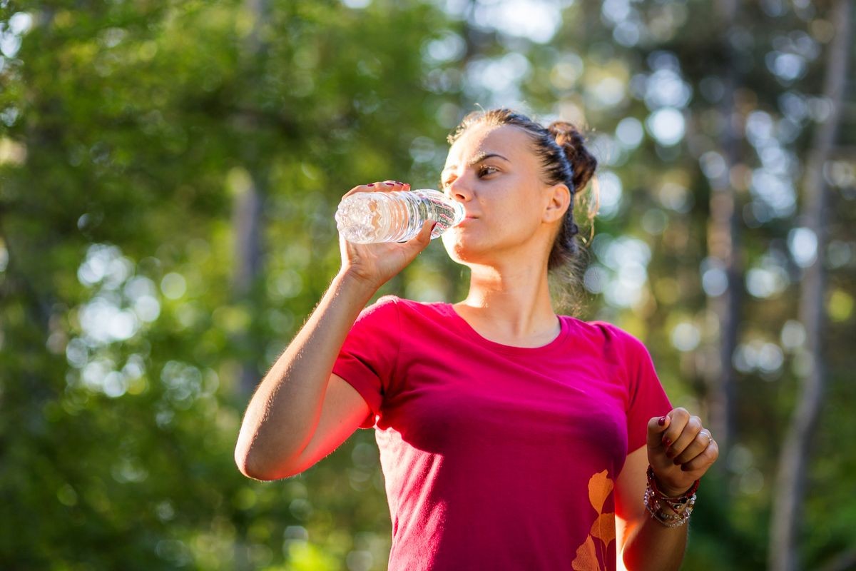 Fit and active attractive young woman drinking water after training outdoor