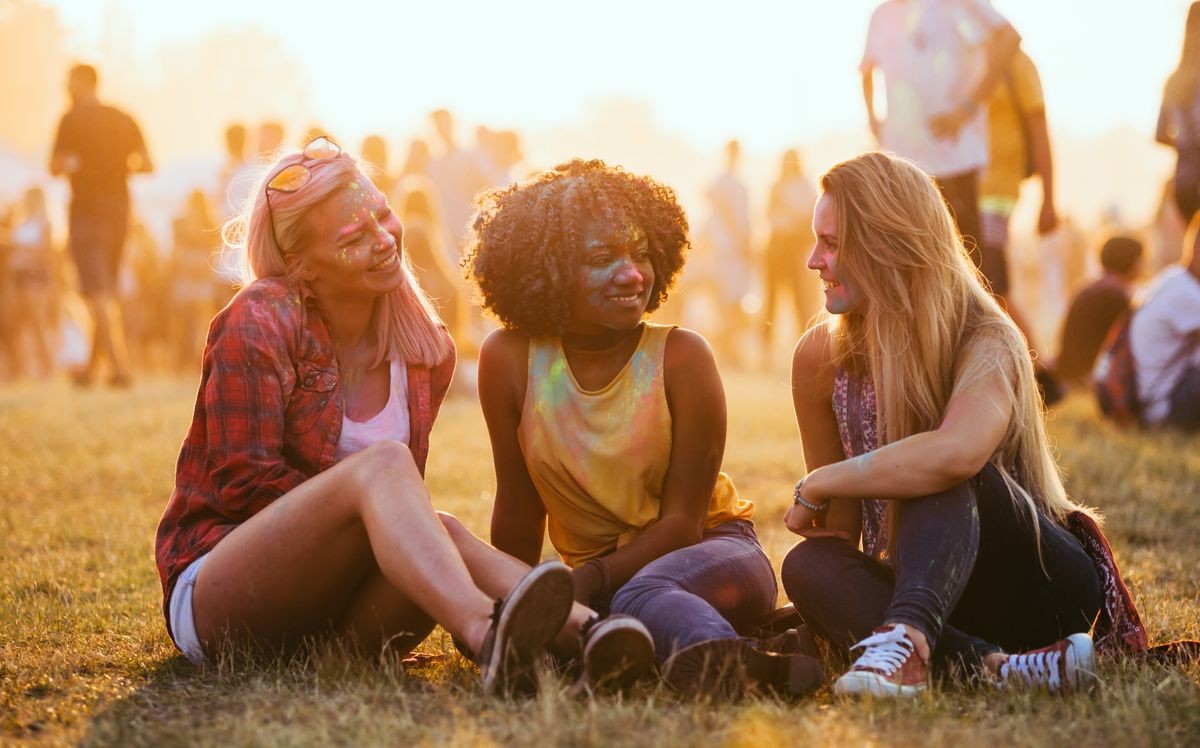 Young multiethnic girls sitting together at summer holi festival