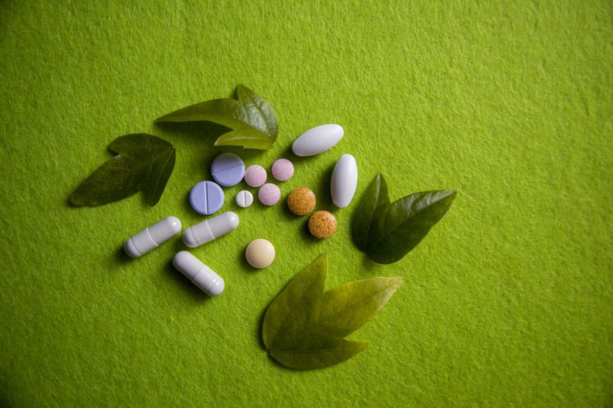 Pharmaceutical medicine pills, tablets and capsules in various colors on light spring green background with fresh green plant leaves. Nature. Top view. Helath care and pharmacy. Copy space for text.