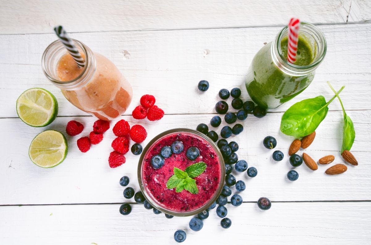 Blueberry, spinach and orange smoothie on a wooden white background. Glasses of smoothie with berry and mint. Berry, leaf and lime, raspberries on a table. Fruit Healthy food. Breakfast.