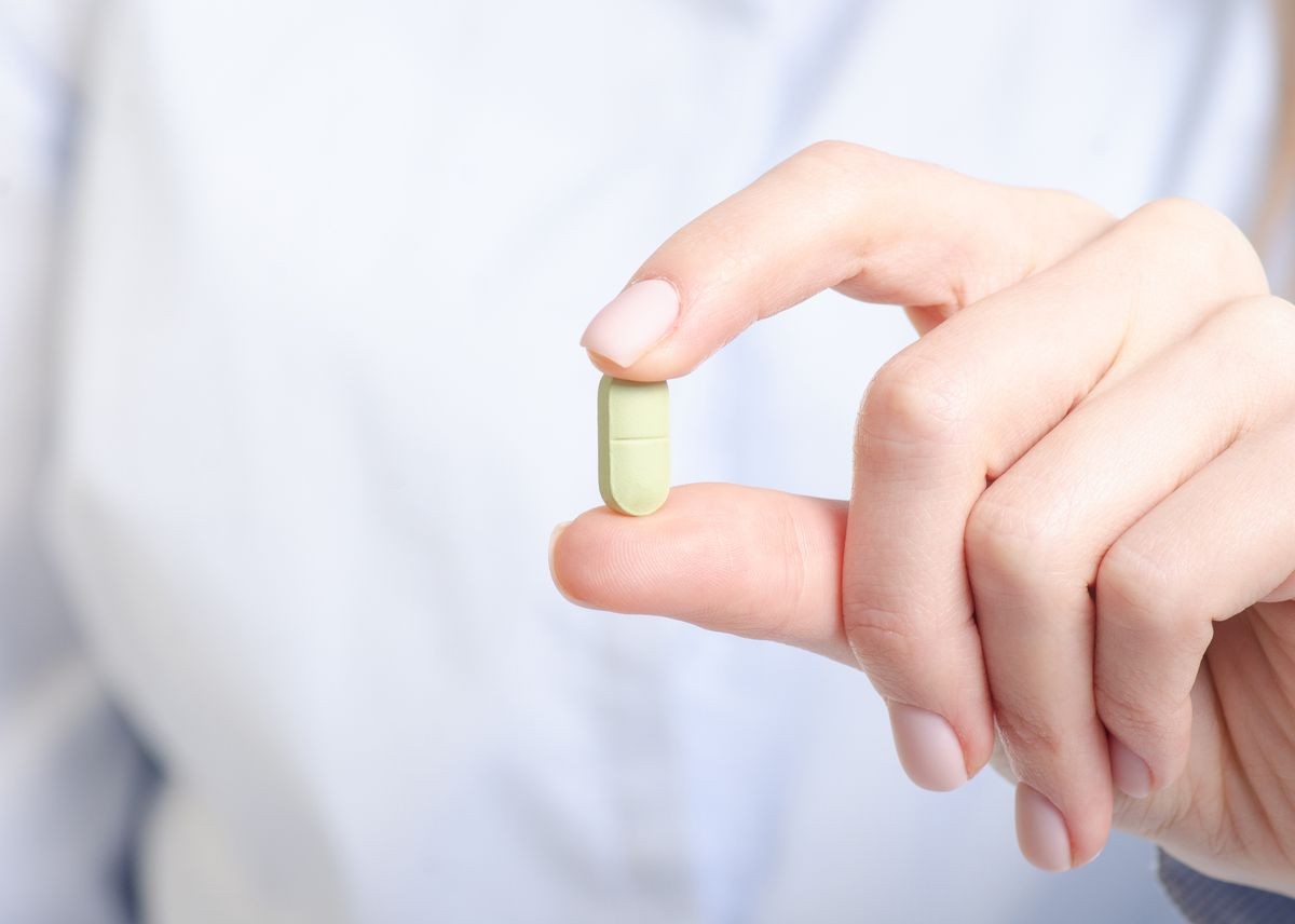 Green capsule pill medicine in woman hand on blur background, pharmacy concept