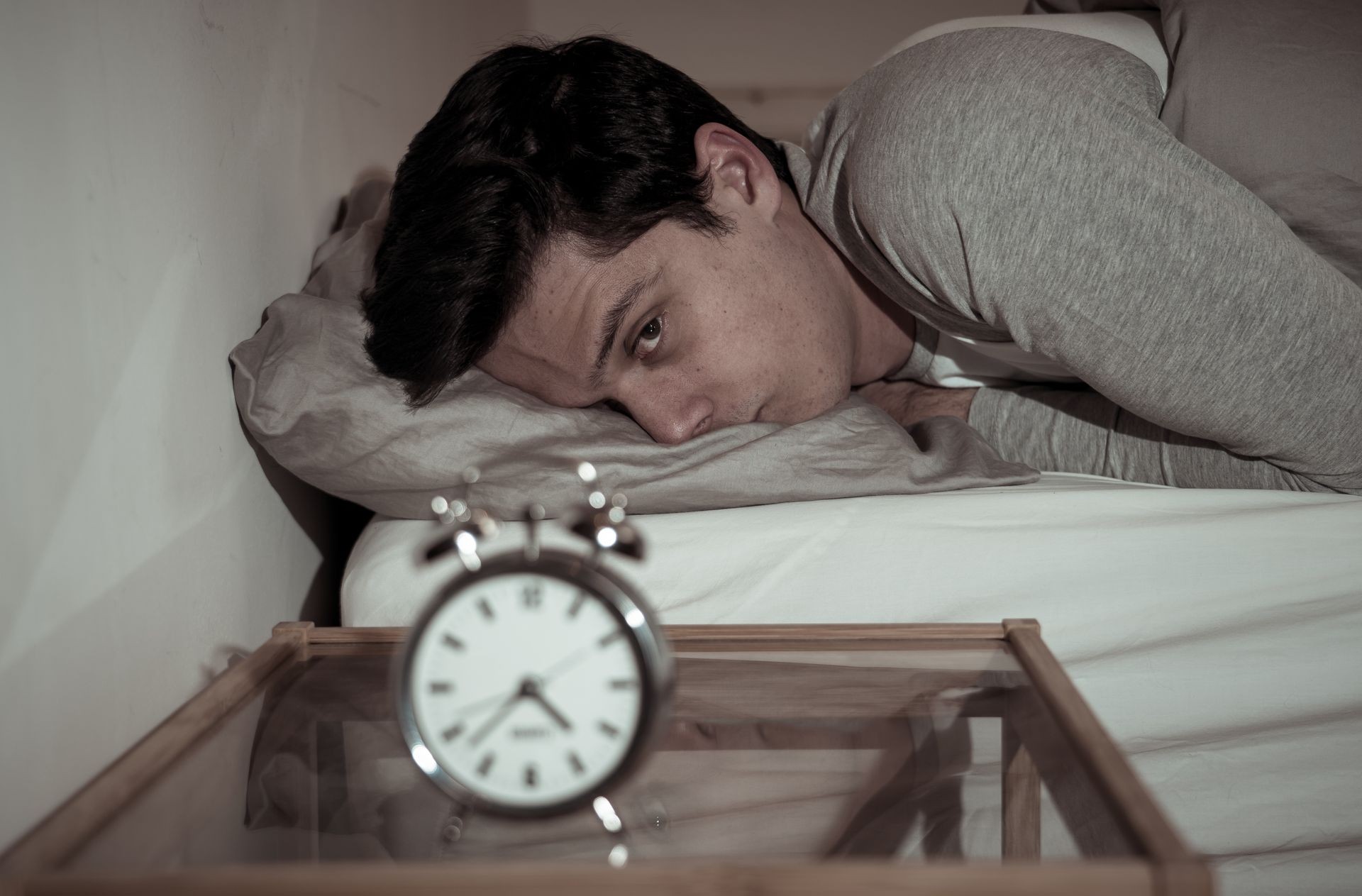 Sleepless and desperate young caucasian man awake at night not able to sleep, feeling frustrated and worried looking at clock suffering from insomnia in stress and sleep disorder concept.