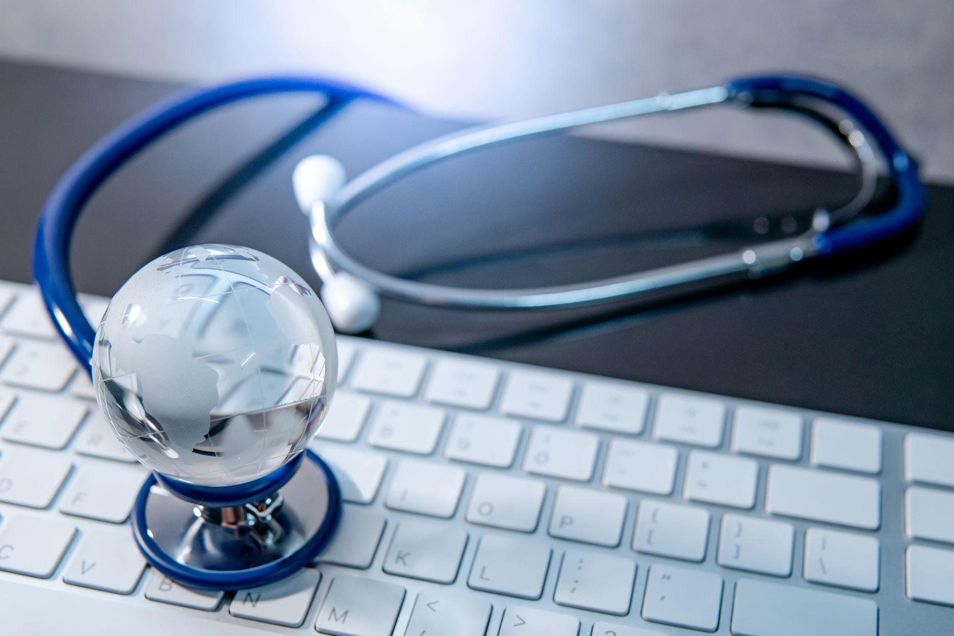 Global healthcare concept. World globe crystal glass on blue stethoscope on white keyboard. Health and medical science. Worldwide wellness business and technology